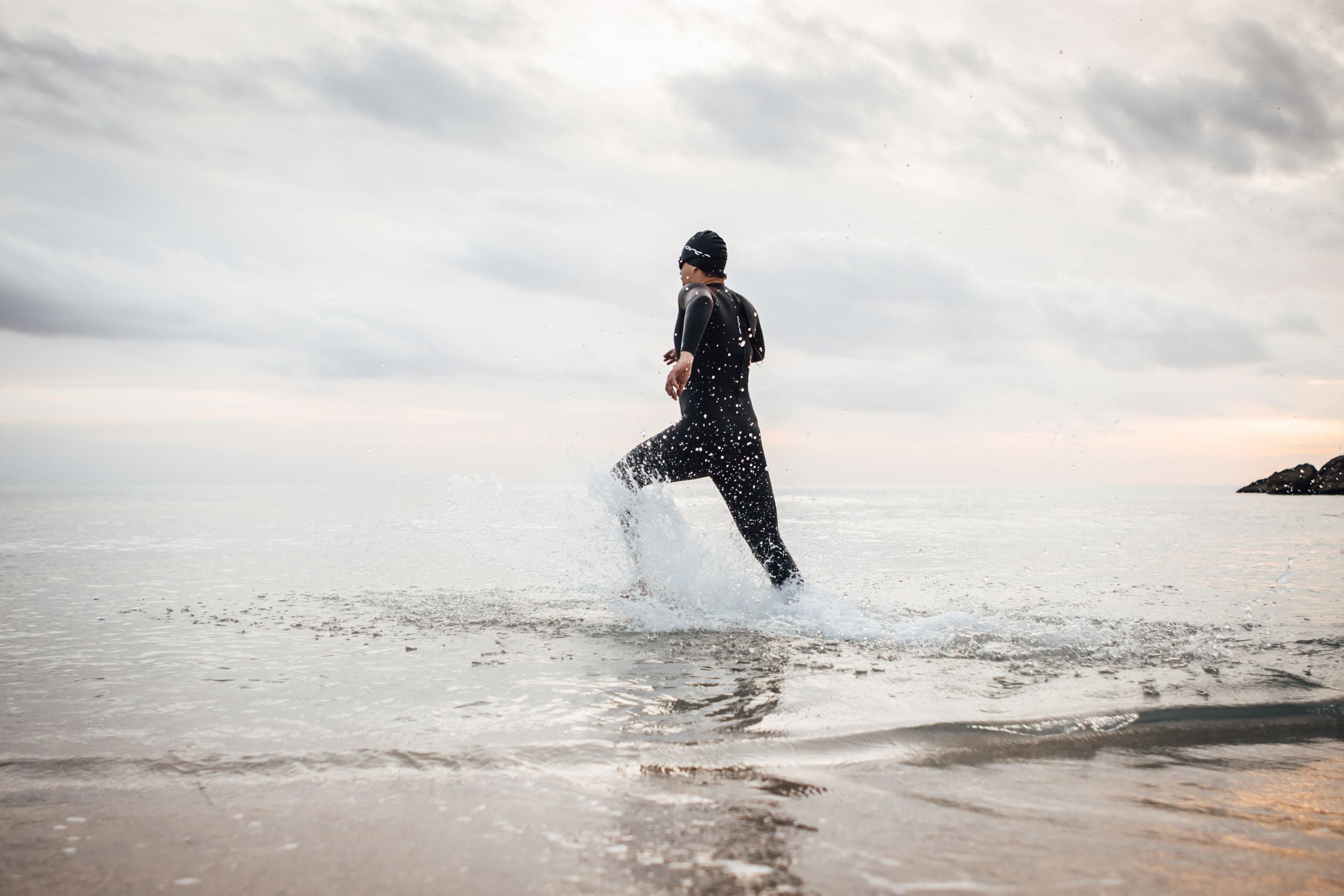 Zwei Triathleten laufen im Neoprenanzug dynamisch in einen See hinein