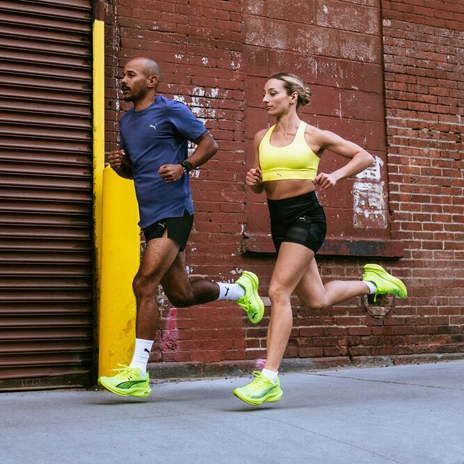 Ein Läufer und eine Läuferin in neoongelben Puma Laufschuhe laufen vor einem Backsteingebäude auf dem Bürgersteig